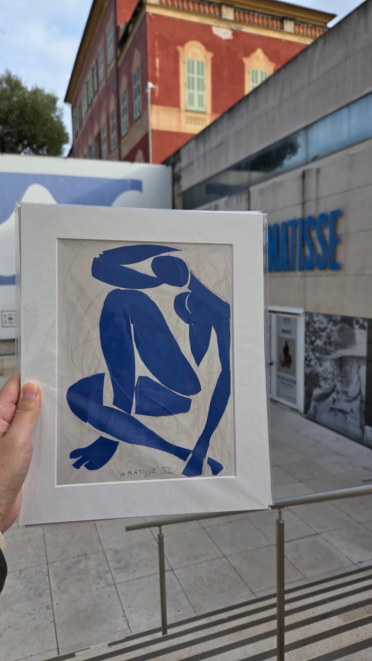 A Henri Matisse blue cut-out print held up in front of the Musee Matisse building facade