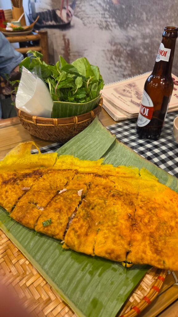 Bánh xèo on a banana leaf, with a basket of herbs and a Hanoi beer